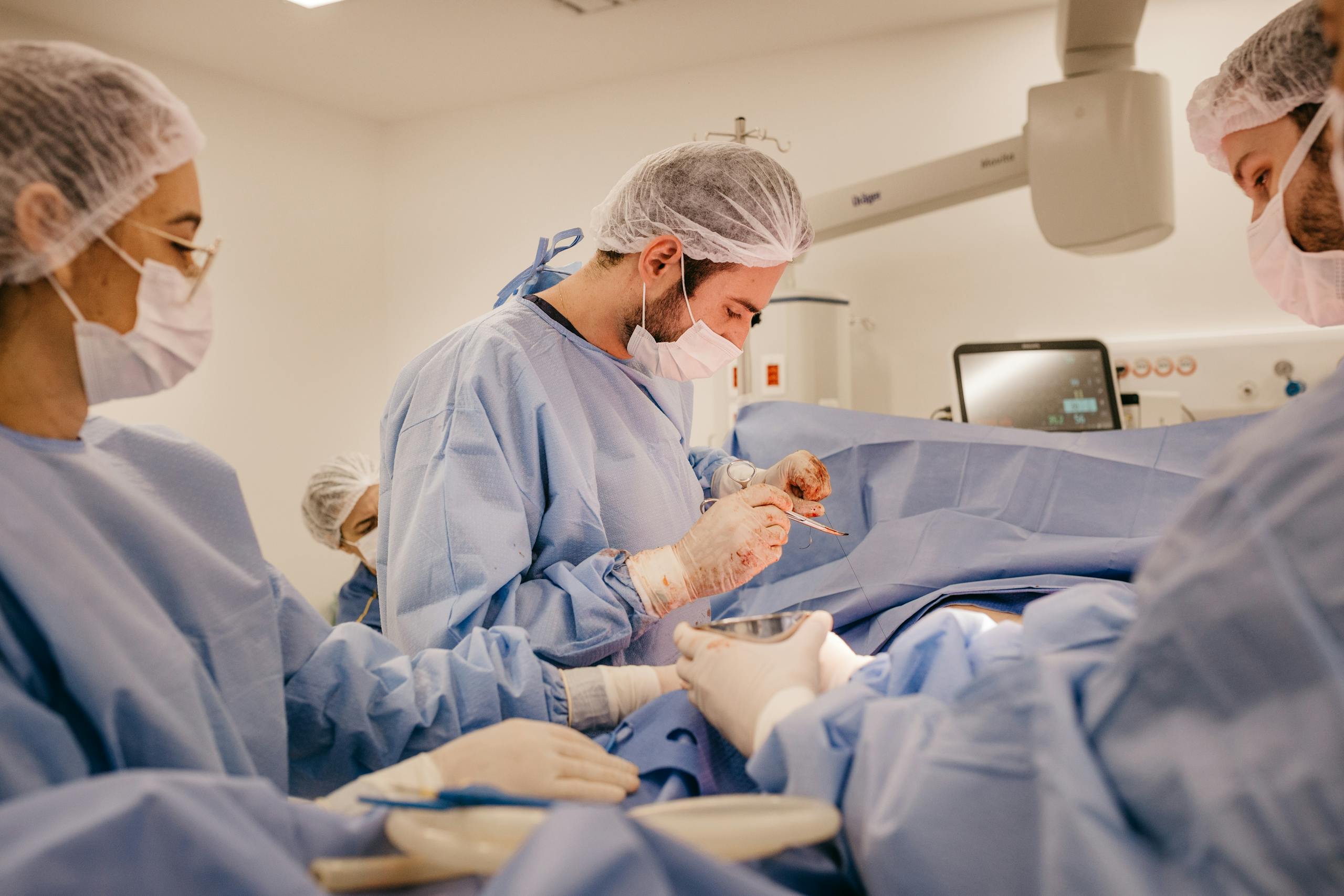 Surgeons and nurses collaborating during a surgical procedure wearing protective gear in a hospital operating room.